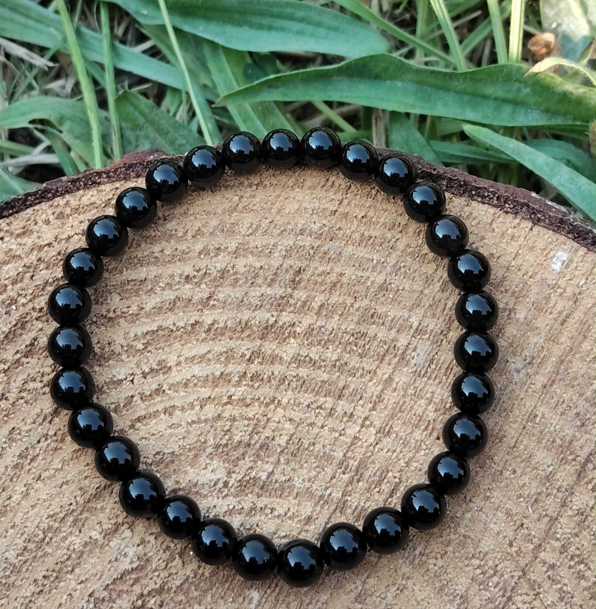Bracelet Onyx noir 6 mm en perles rondes sur élastique, décor bois et herbes vertes floues, endurance, volonté et clarté mentale.