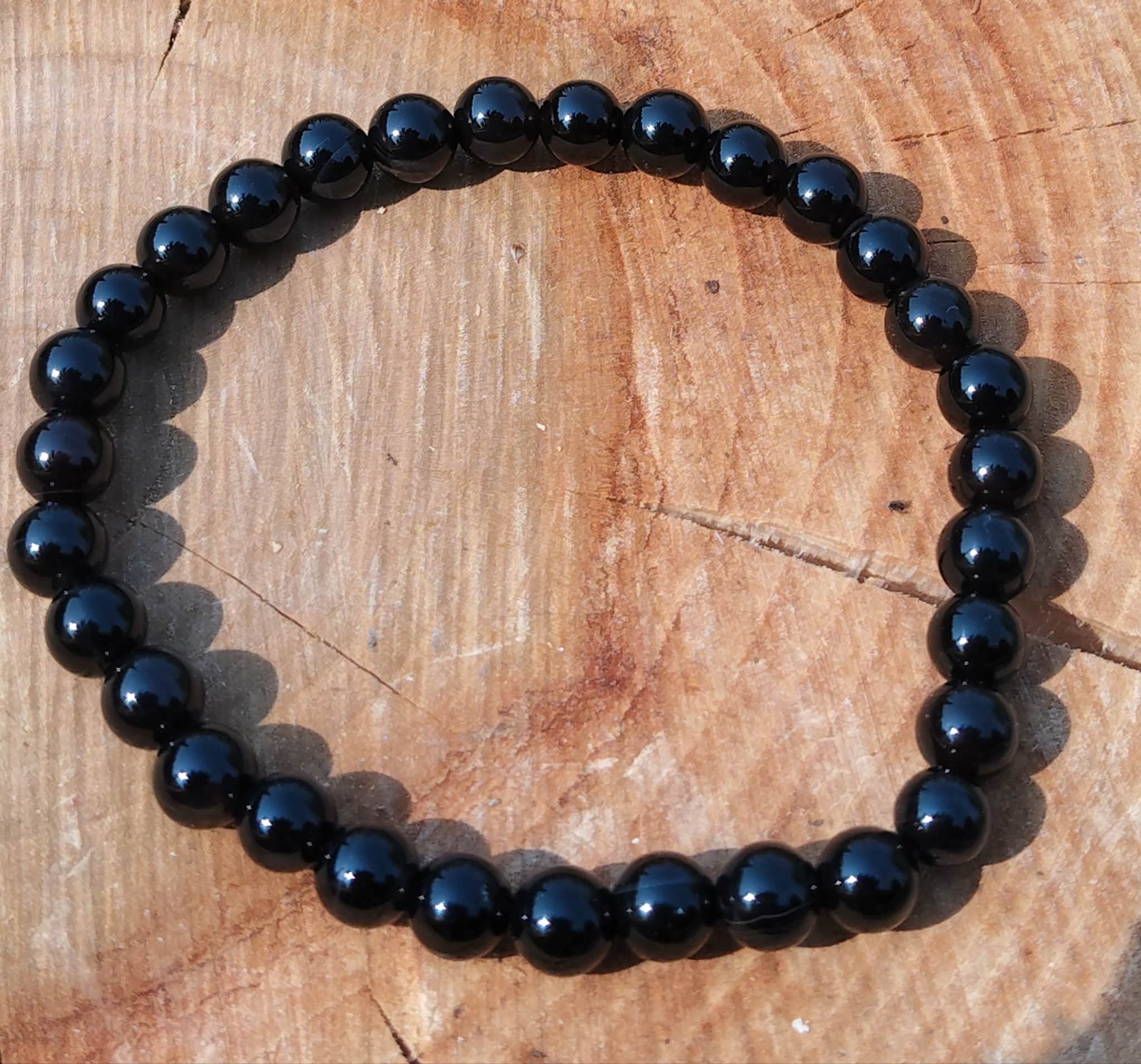 Bracelet Onyx noir en perles lisses rondes, vue du dessus en décor naturel, recentrage, lucidité et maîtrise émotionnelle.
