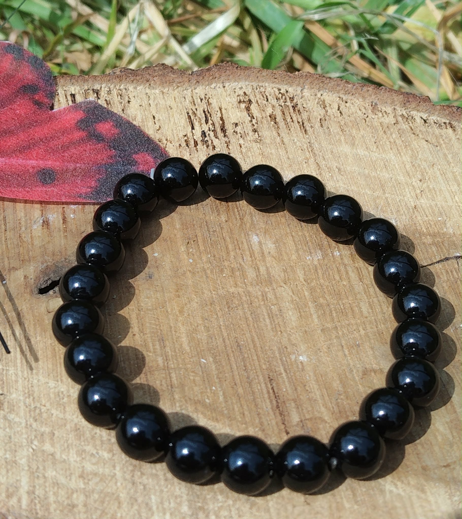 Bracelet Onyx noir 8 mm en perles noires lisses sur bois naturel et fond végétal, assurance, persévérance et lucidité.