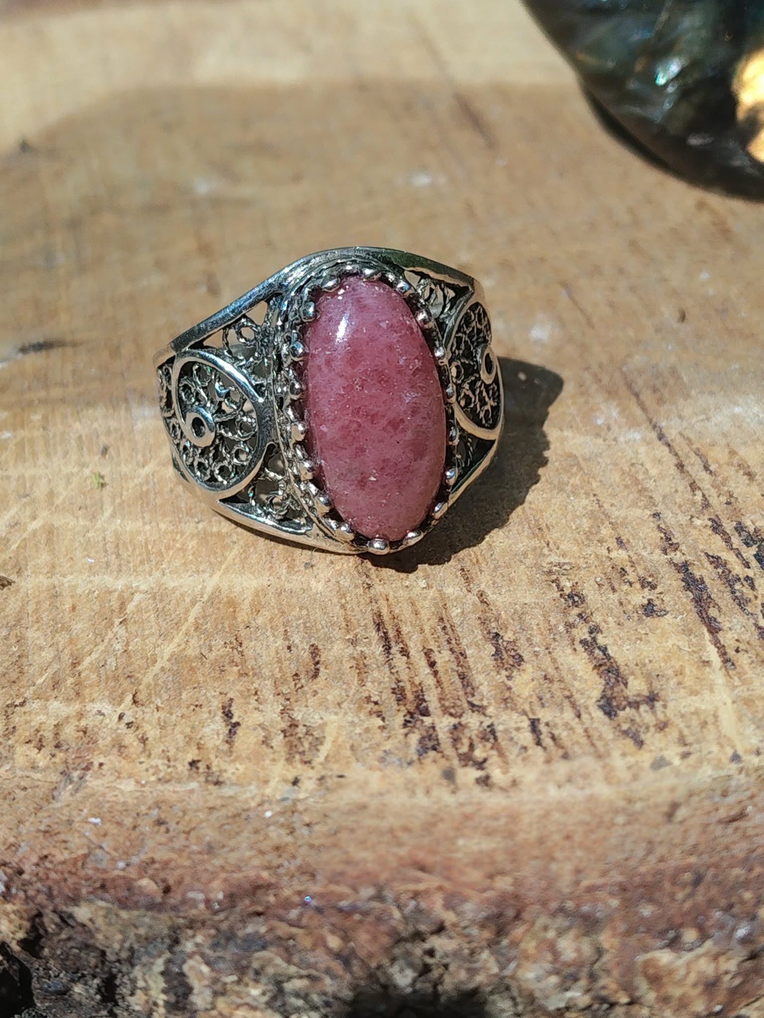 Bague rhodonite cabochon ovale rose filigrane argent 925 posée sur rondin de bois décor nature intentions associées apaisement équilibre émotionnel compassion