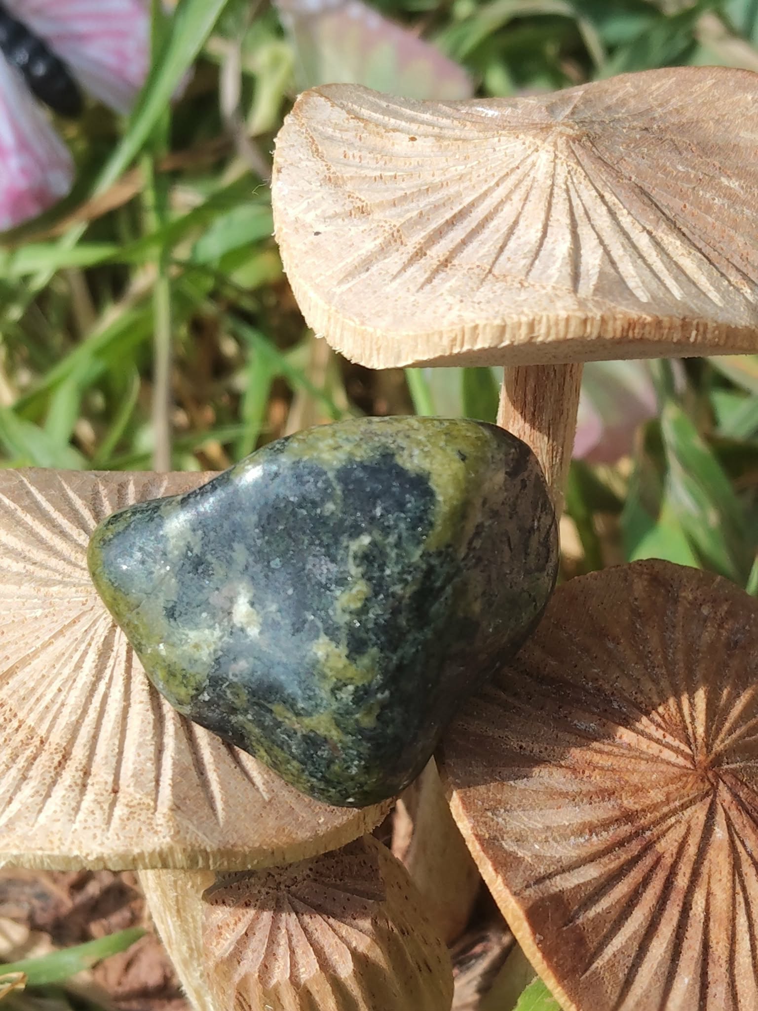 Pierre roulée de serpentine vert foncé, sur champignons en bois gravé et feuillage; apaisement, ancrage, équilibre émotionnel.