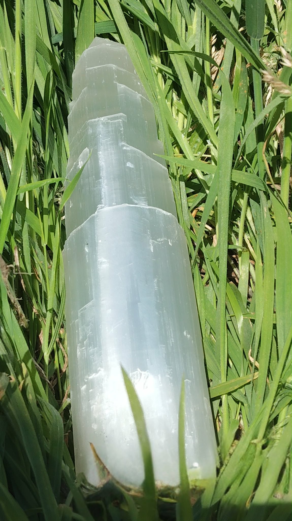 Tour en sélénite blanche polie posée dans l’herbe, prise de vue rapprochée, lumière naturelle, pour une énergie légère et atmosphère zen.