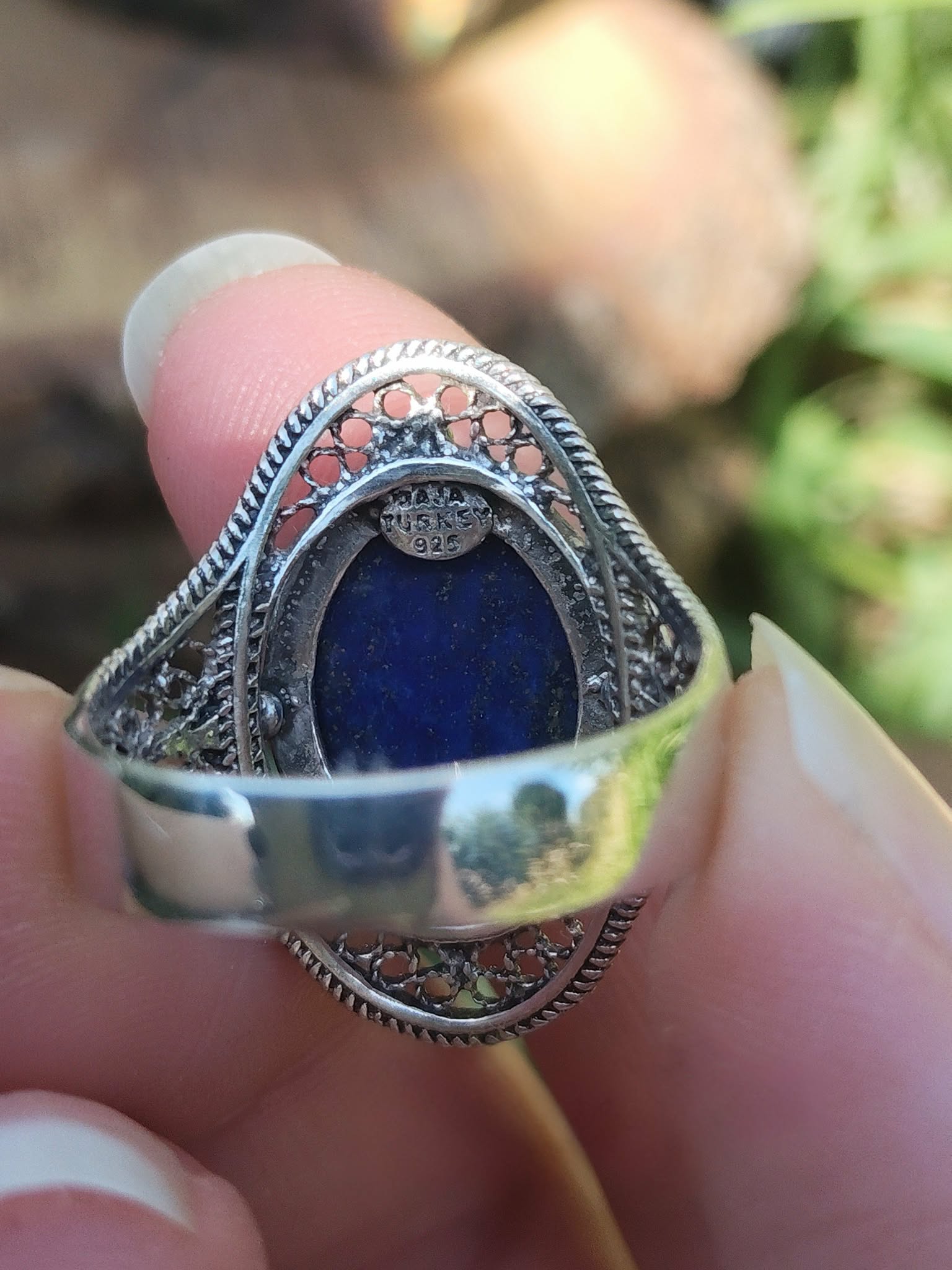 Vue arrière d’une bague argent 925 filigranée avec lapis lazuli bleu, tenue entre les doigts, pour soutenir confiance, clarté et communication.