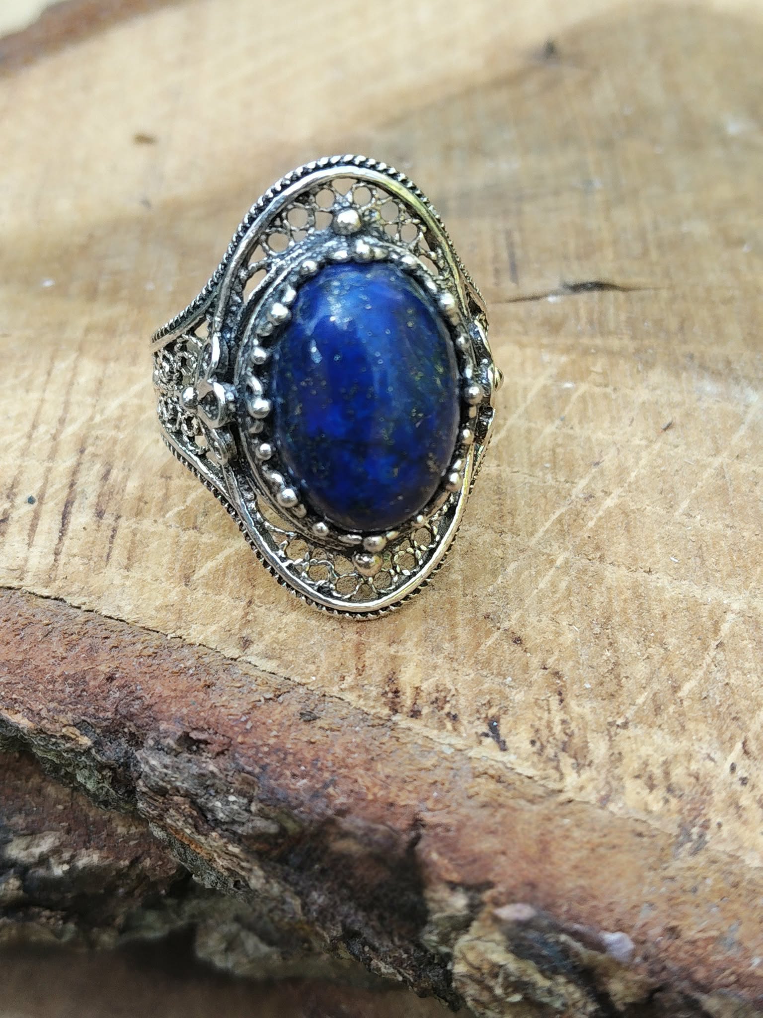 Bague filigranée en argent 925, lapis lazuli bleu intense, présentée sur bois veiné, pour lucidité, calme et harmonie.