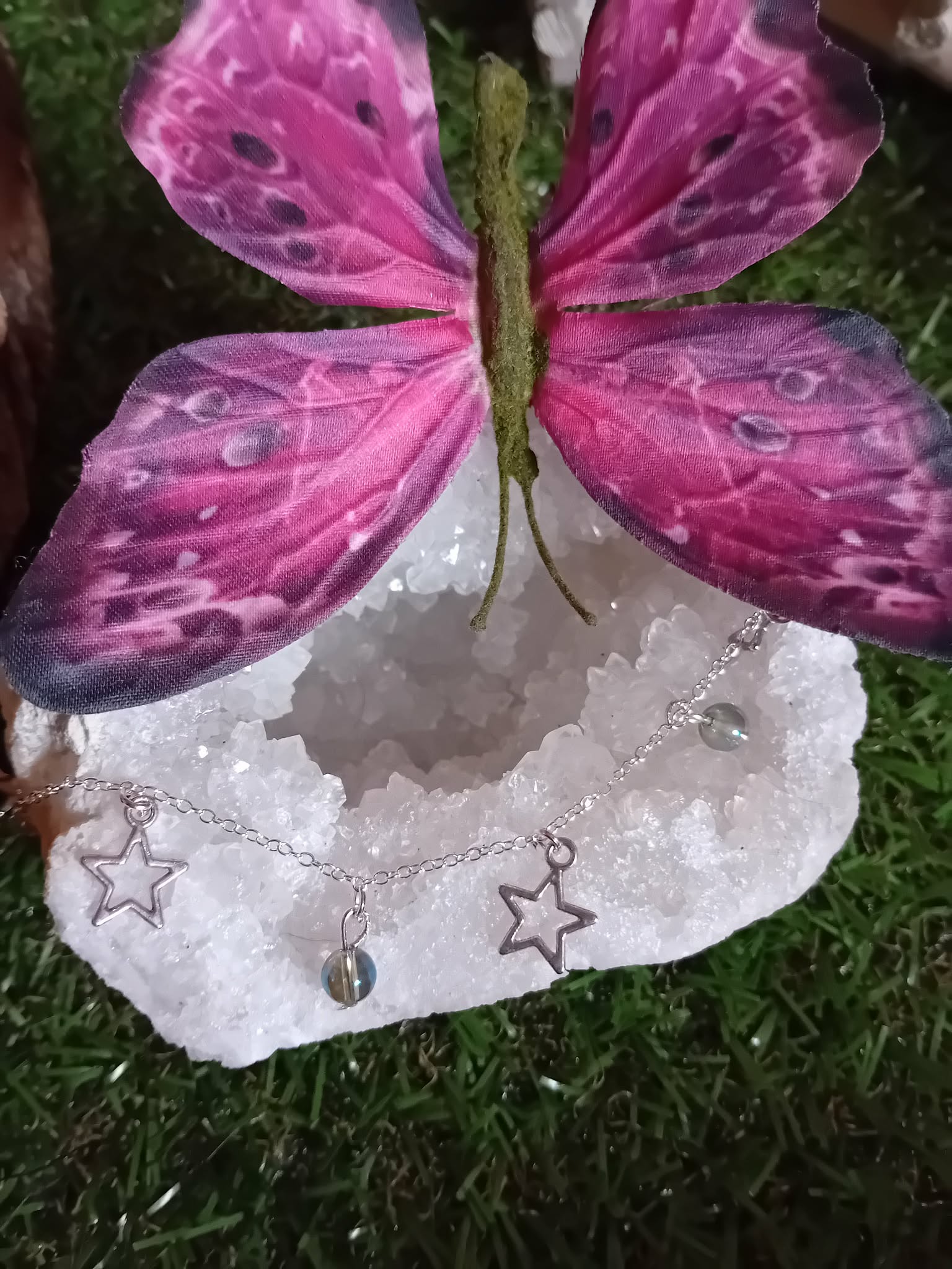 Chaîne de cheville création Magic Gaïa en acier inoxydable, étoiles et perles Aqua Aura, posée sur un cristal blanc sous un papillon rose, pour une touche de fraîcheur et confiance.
