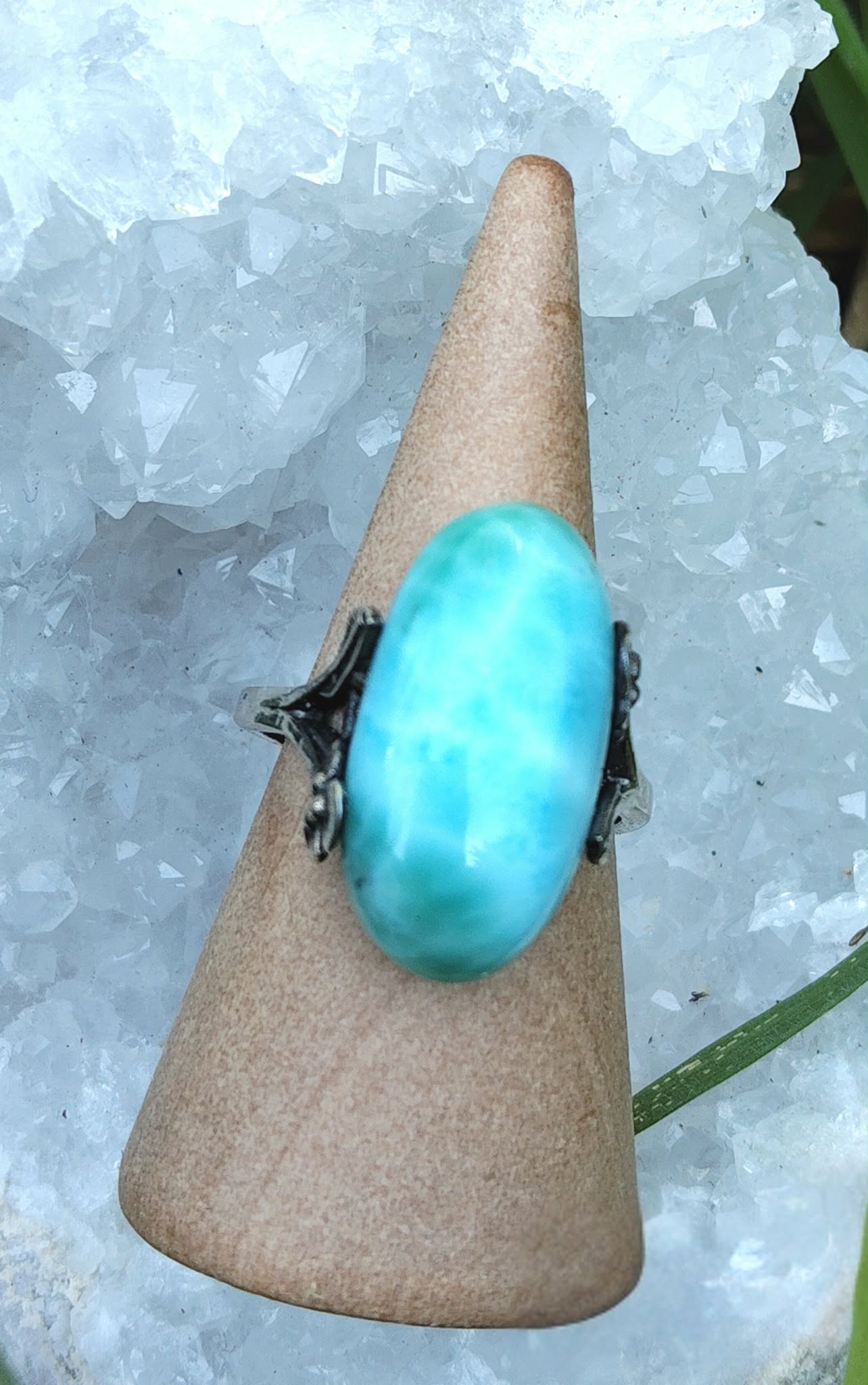Bague réglable en argent avec cabochon de larimar bleu, posée sur un présentoir conique devant des cristaux givrés, pour apaiser, clarifier et inviter la douceur.