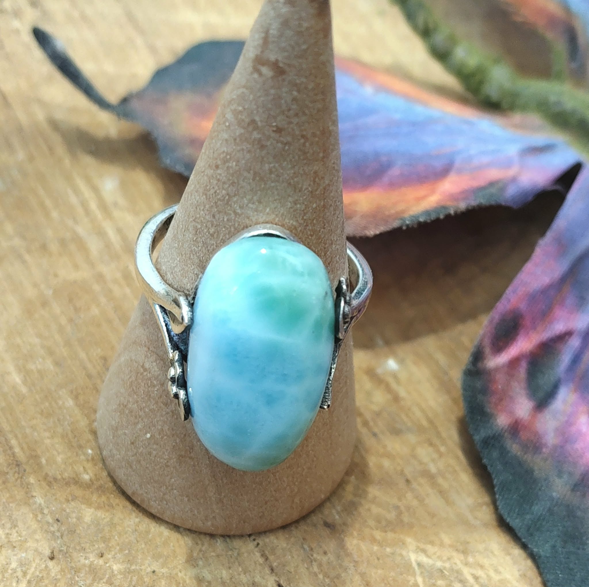 Bague larimar réglable en argent, sur cône en kraft posé sur bois, ailes de papillon irisé en décor, pour apaisement, clarté et expression.