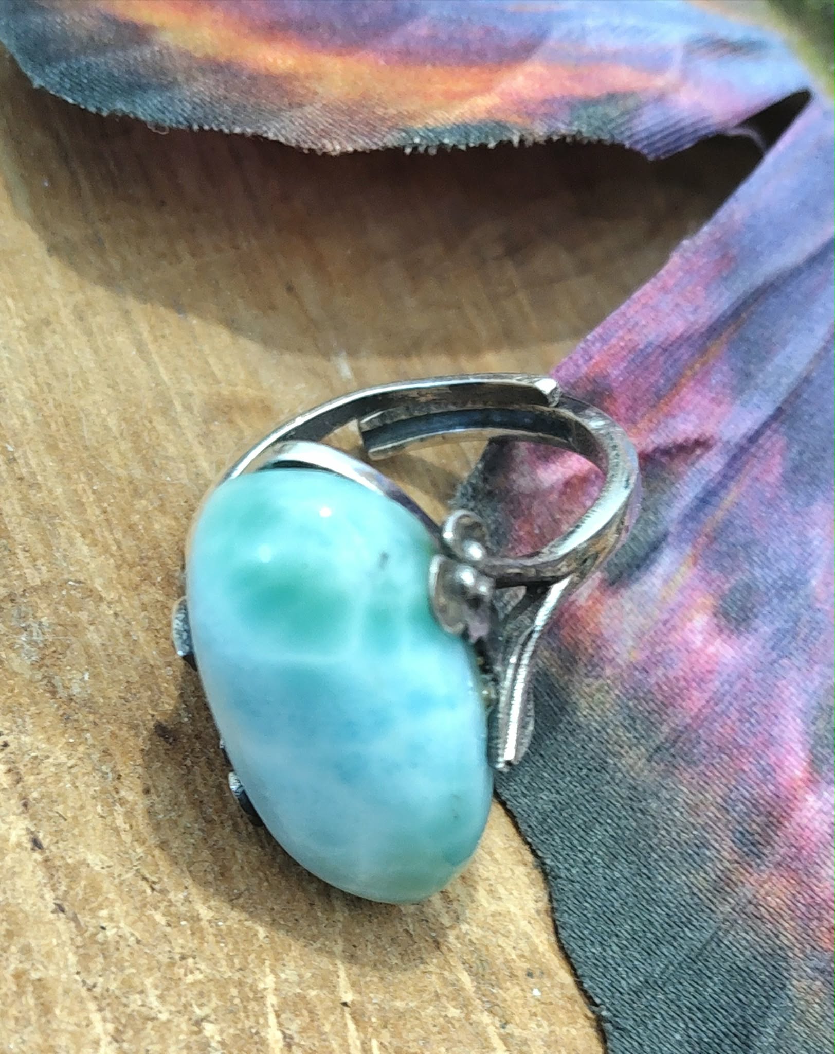 Bague réglable en argent avec larimar bleu lagon, posée sur rondin de bois près d’une aile de papillon irisée, pour douceur, apaisement et expression.