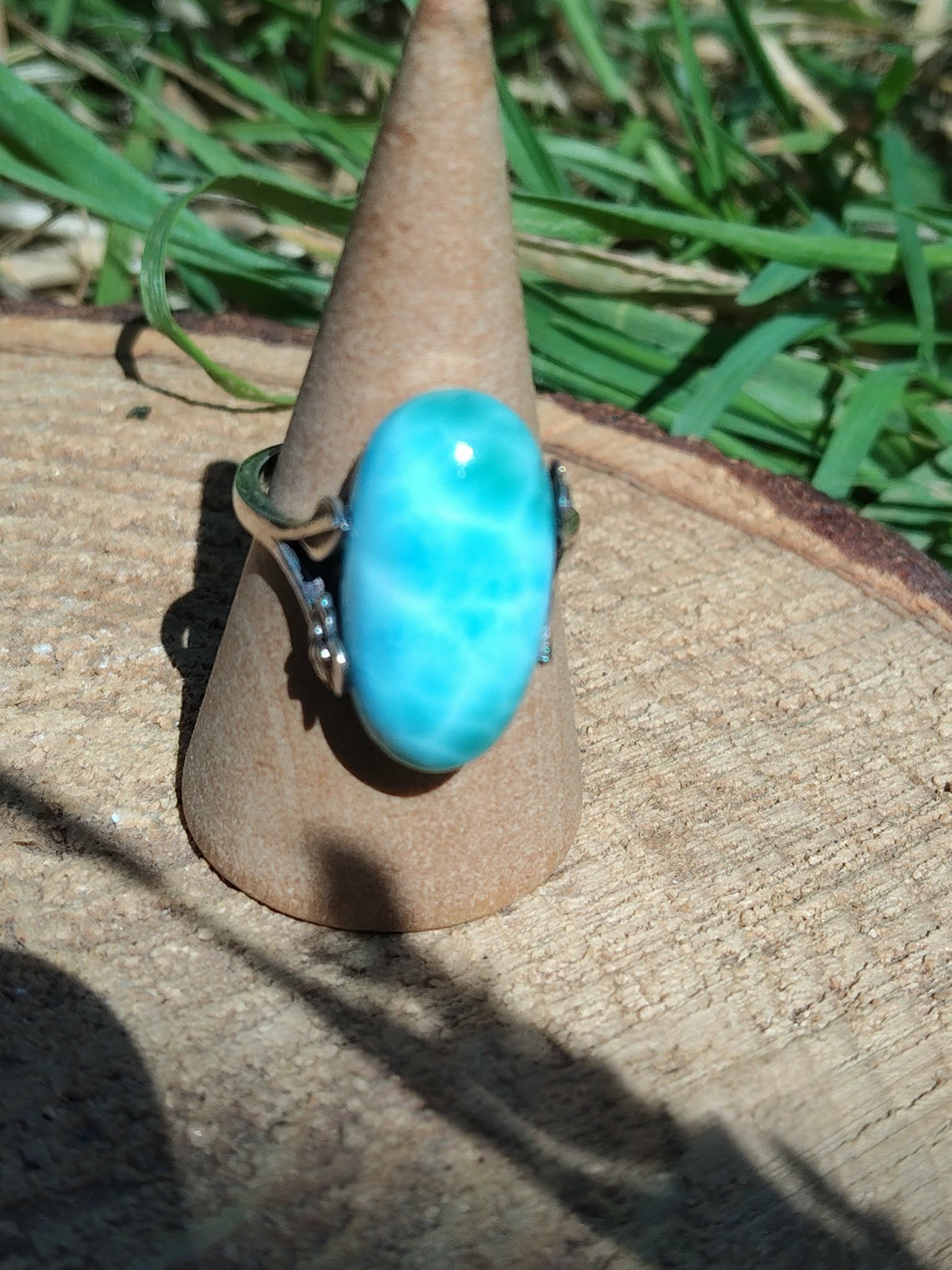 Bague larimar réglable en argent sur cône en kraft, posée sur table en bois au soleil avec feuillage flou, pour calme, clarté et confiance.