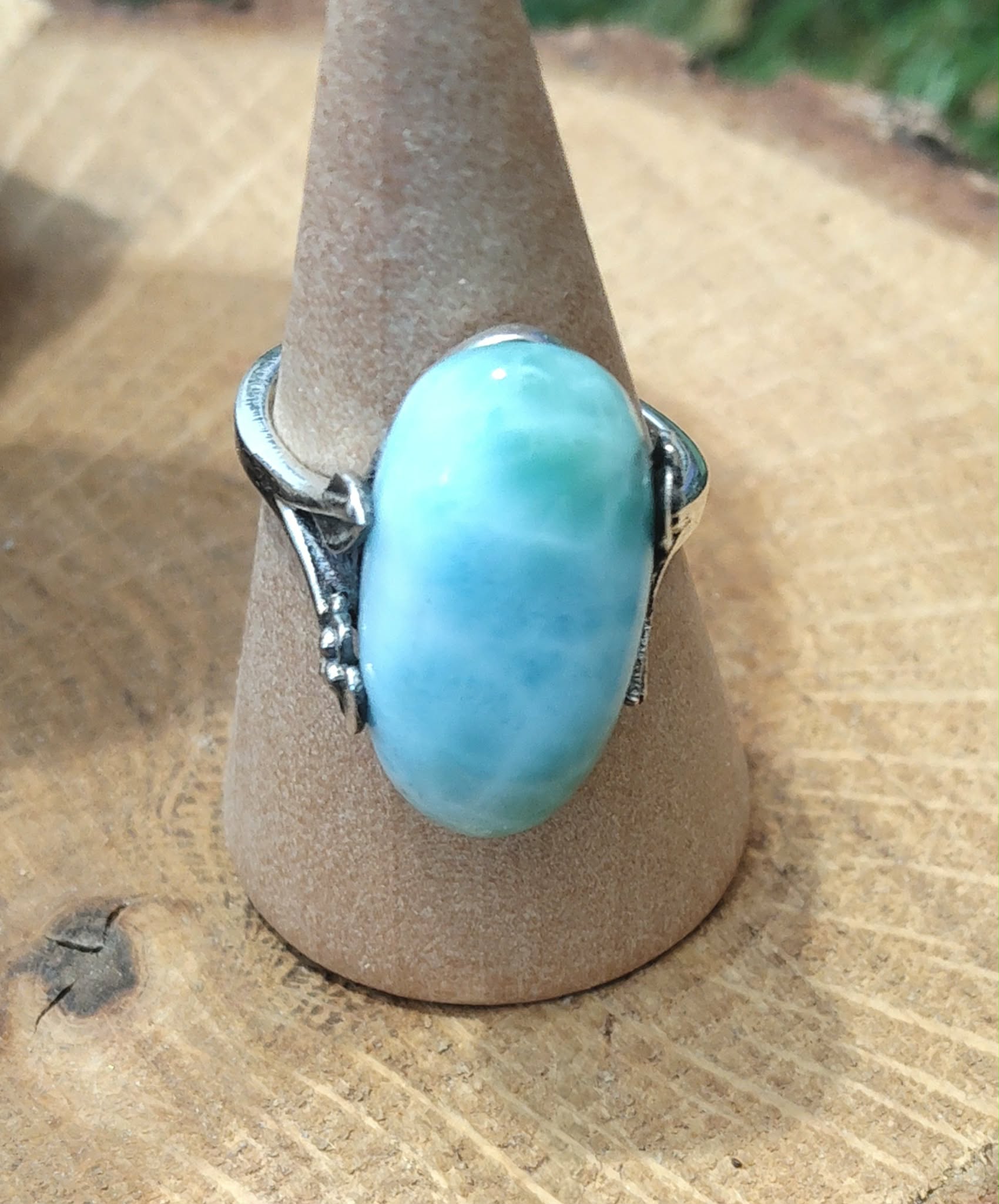 Bague larimar en argent réglable sur support conique, posée sur bois naturel avec touche de verdure, pour douceur et calme intérieur.