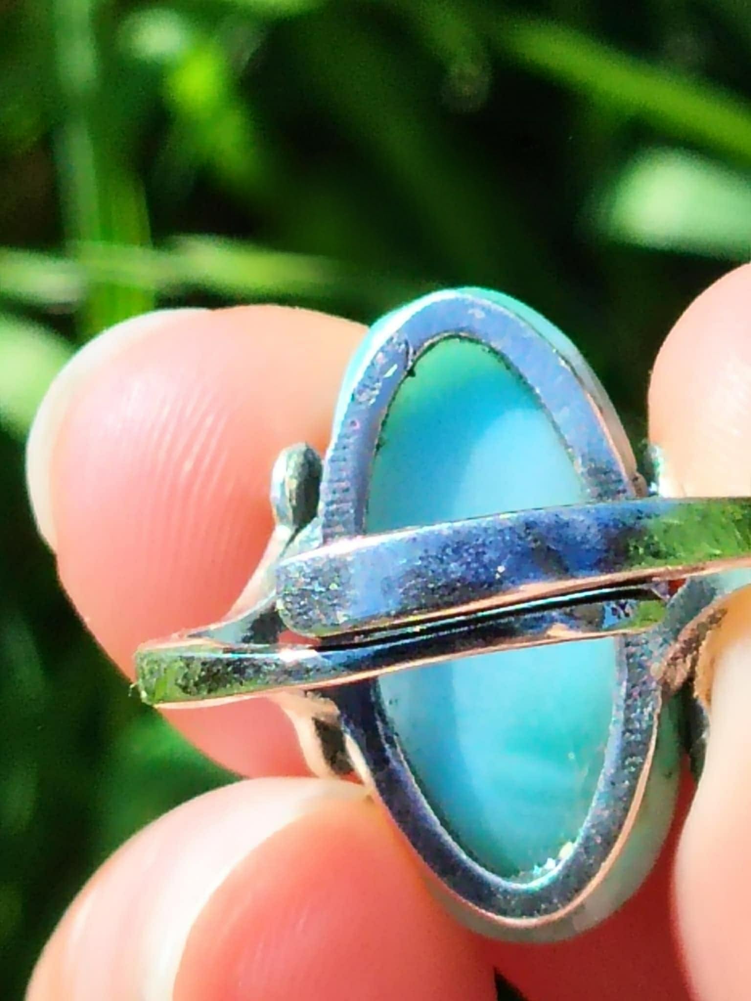 Vue arrière de la bague larimar en argent réglable, tenue entre les doigts avec une tige dherbe, fond vert flou, pour apaiser et exprimer sa vérité.