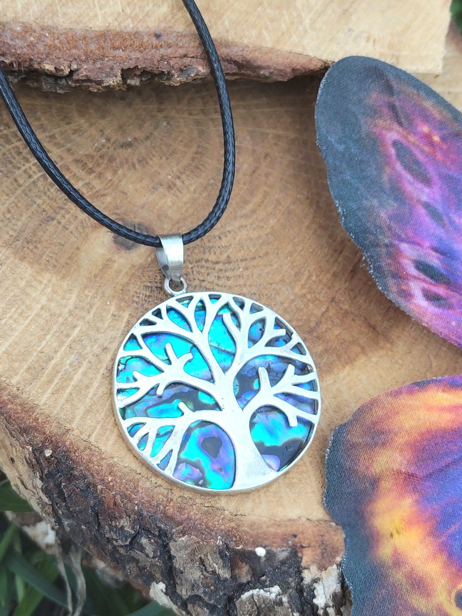 Pendentif arbre de vie en abalone et argent 925 sur cordon noir, posé sur rondin de bois avec papillon décoratif, bijou en nacre naturelle associé à l’harmonie émotionnelle, à la tranquillité et à la douceur intérieure.
