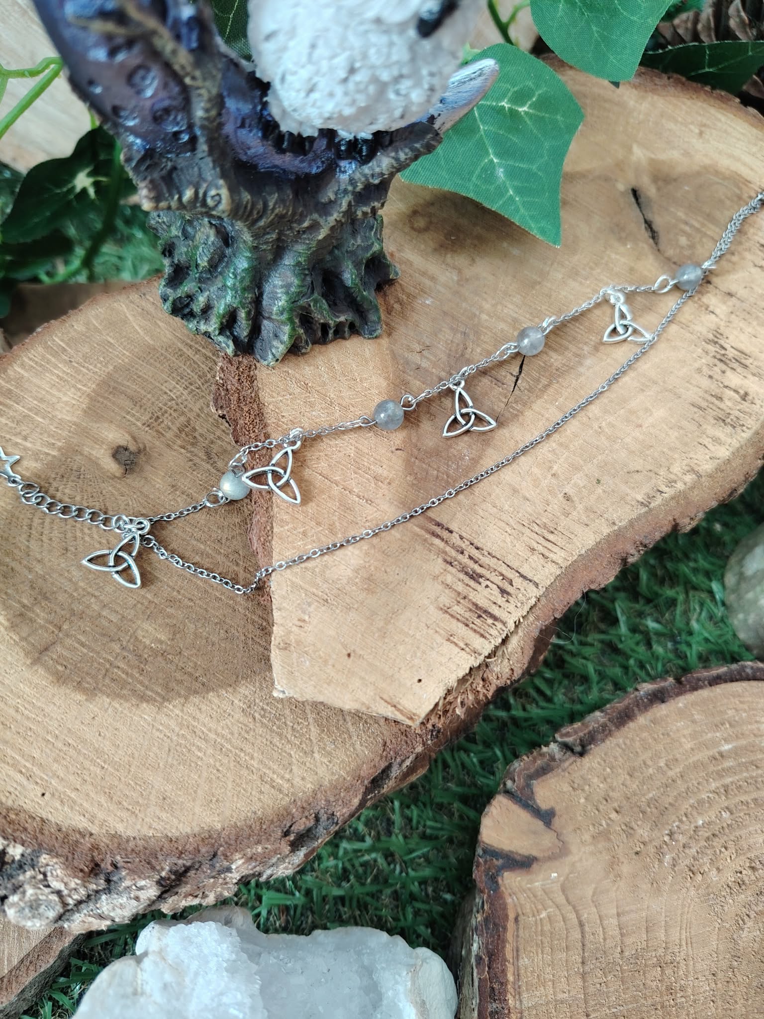 Chaîne de cheville en acier inoxydable, création Magic Gaïa, avec triquetra et perles de labradorite, posée sur rondins de bois et mousse avec papillon décoratif, pour une touche de protection et confiance