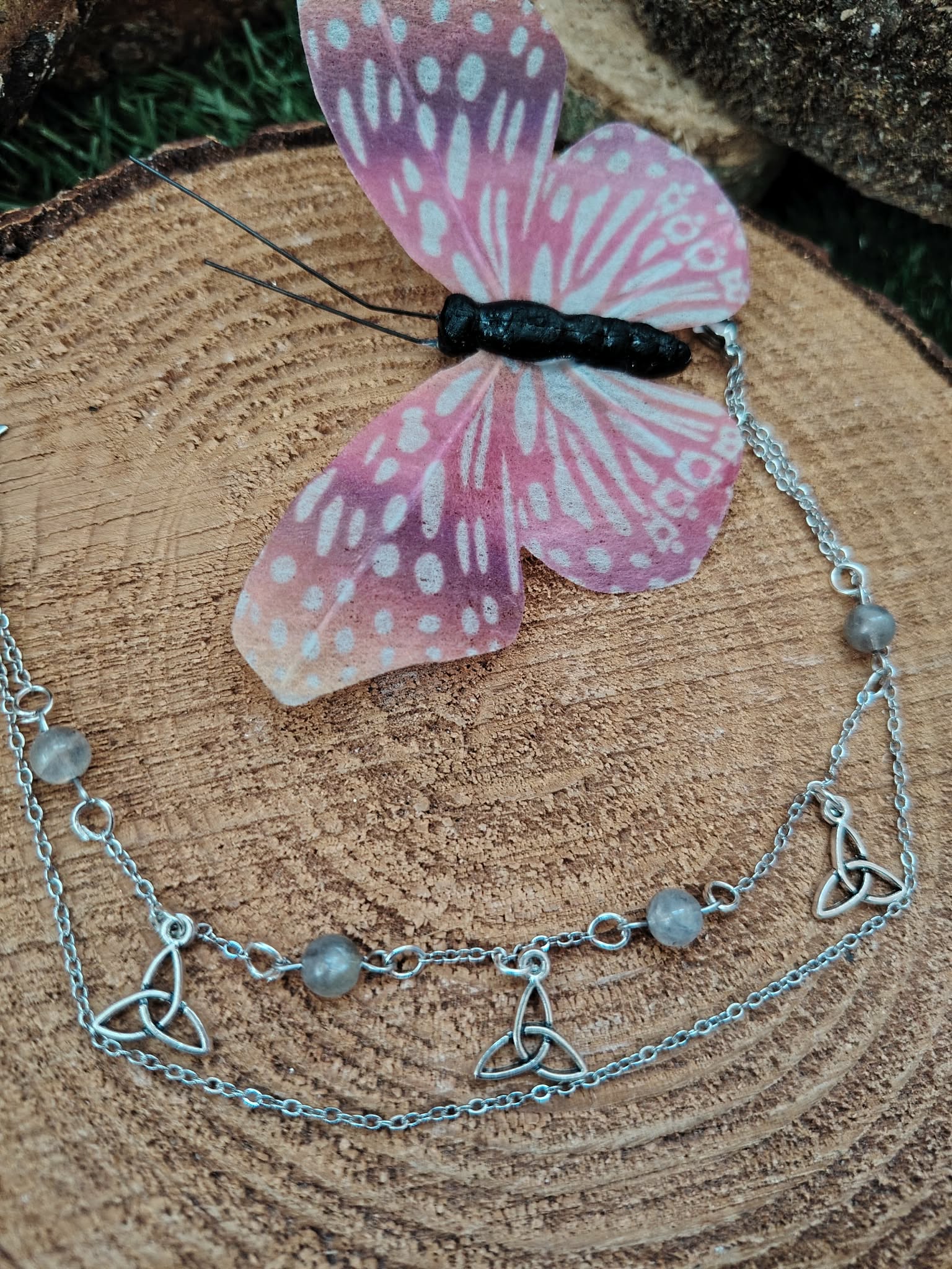 Chaîne de cheville création Magic Gaïa en acier inoxydable, breloques étoiles et perles de labradorite, posée sur rondin de bois avec papillon décoratif, pour une touche de protection et d’assurance.