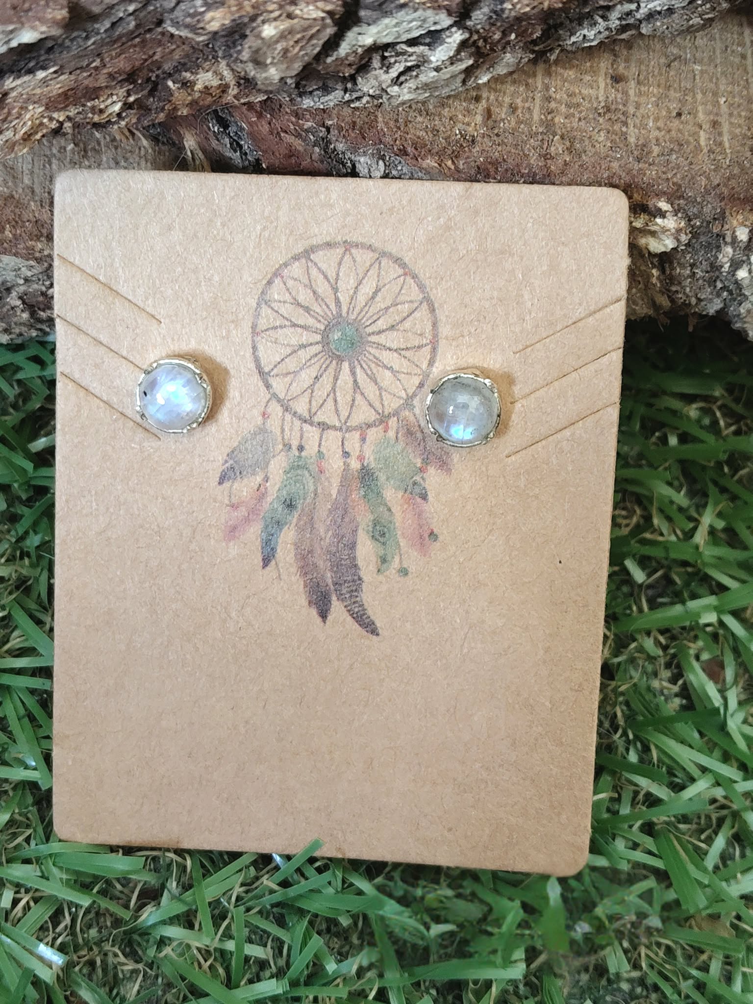 Puce d’oreilles en argent 925 avec péristérite aux reflets bleus, posées sur carte attrape-rêves sur mousse verte et bois brut, pour apaiser et clarifier l’esprit.
