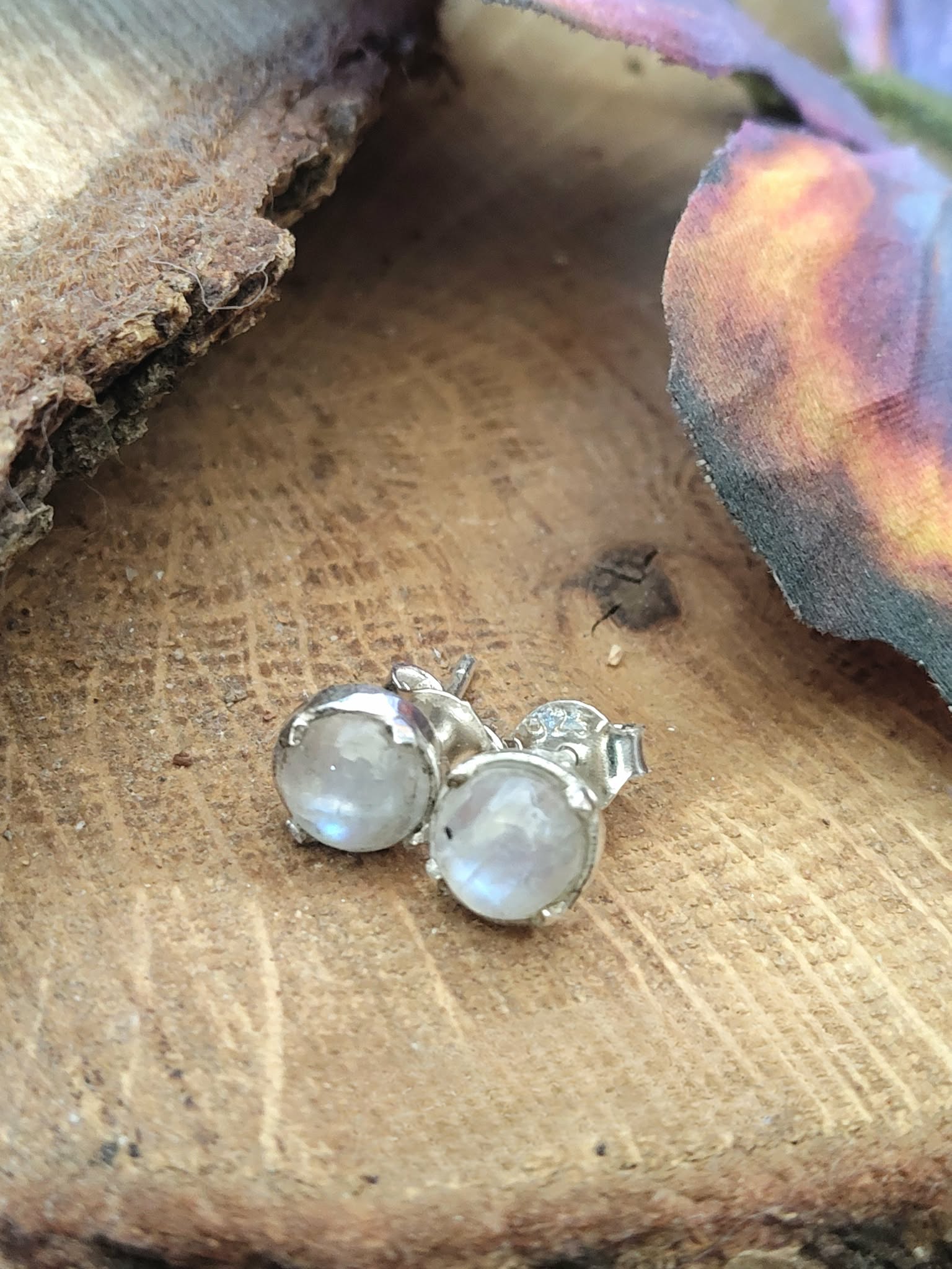 Boucles d’oreilles puces en argent 925 avec péristérite, posées sur rondin de bois avec aile de papillon floutée, pour douceur, intuition et sérénité.