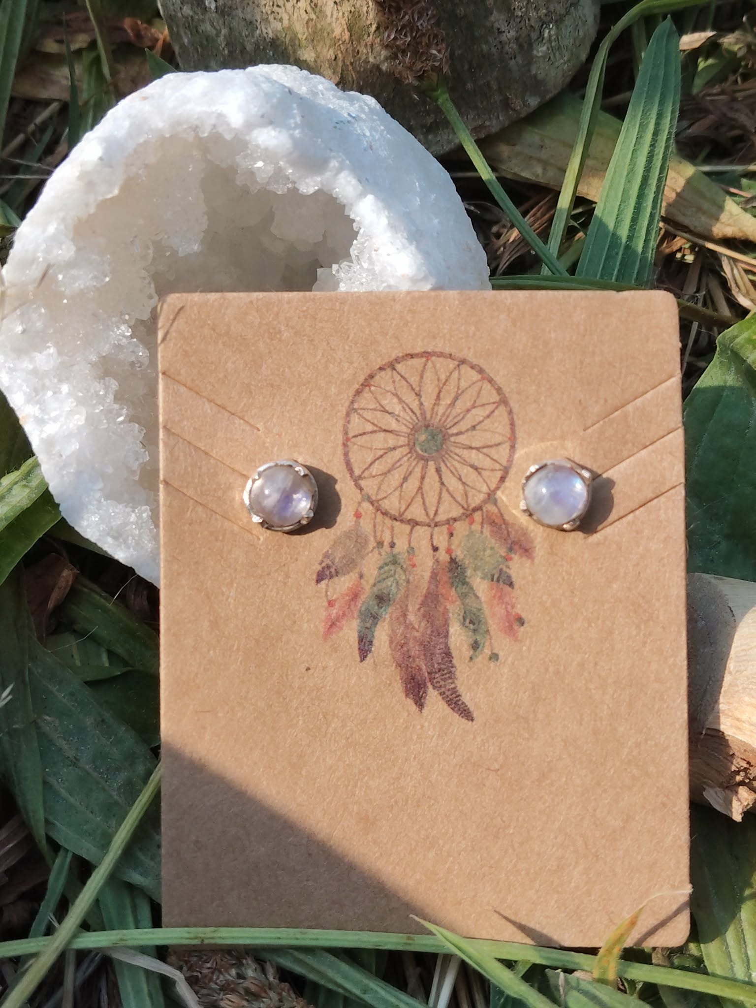 Boucles d’oreilles puces en argent 925 avec péristérite sur carte kraft attrape-rêves, posées dans l’herbe près d’une pierre blanche, pour douceur et intuition
