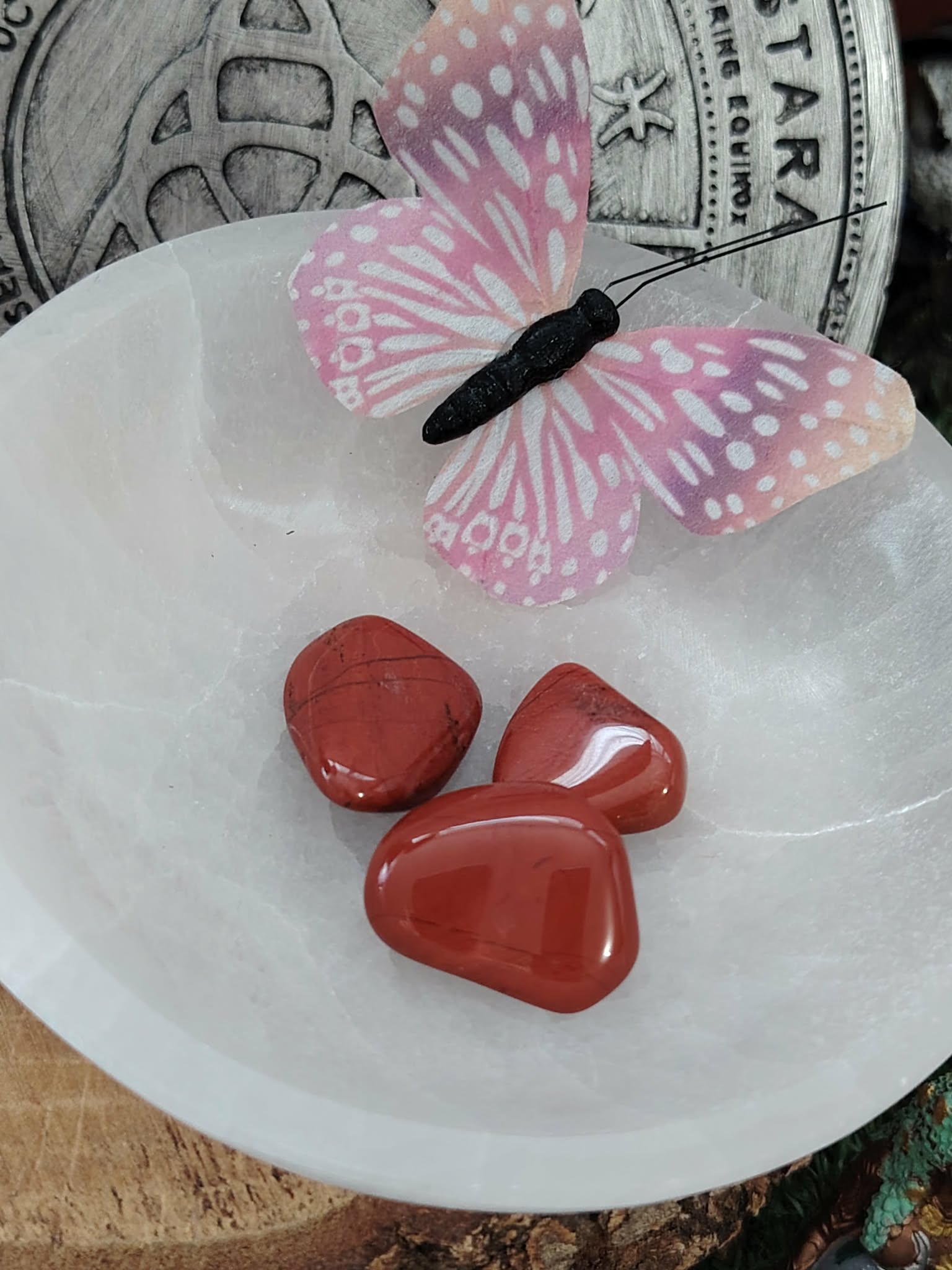 Bol en sélénite blanche 15 cm sur rondin de bois, jaspe rouge roulé et papillon rose, planche Ostara en fond, pour ancrage et clarté.