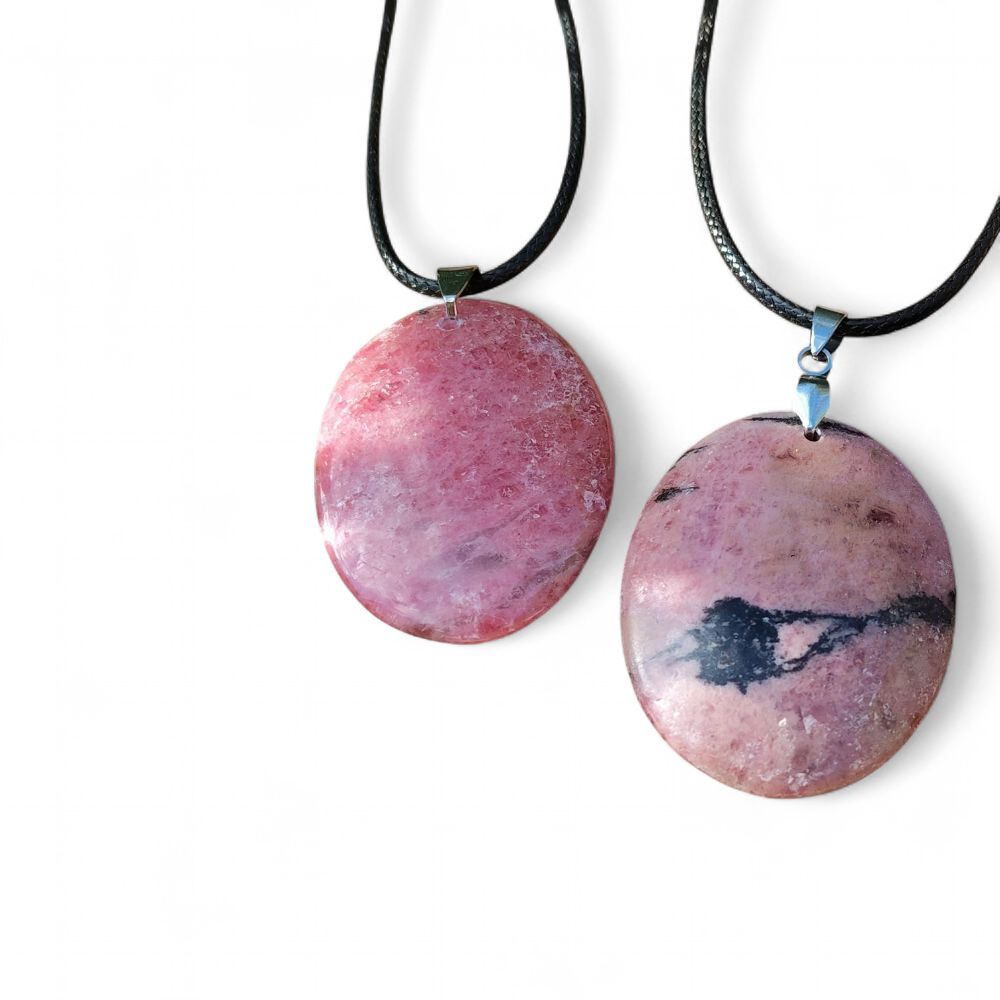 Deux pendentifs ronds en rhodonite sur cordons noirs, photographiés sur fond blanc, bijoux en pierre naturelle reliés à l’apaisement, à la tendresse et à l’harmonie intérieure.