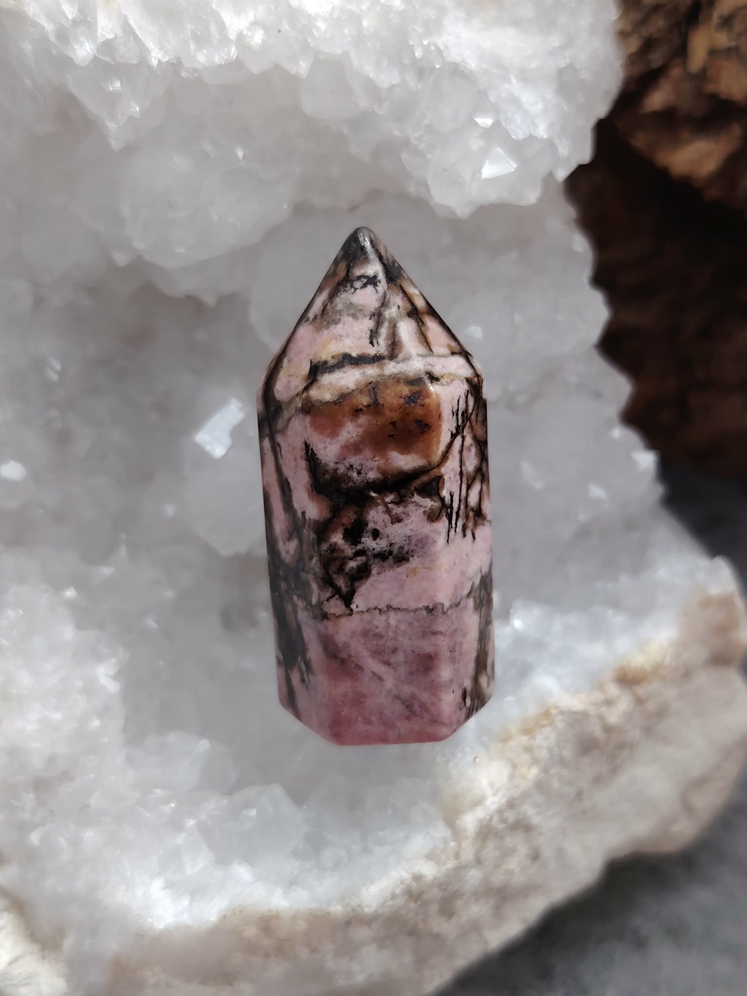 Pointe de rhodonite rose veinée de noir posée dans un bol de sélénite blanc, lumière douce et fond sombre, pour apaiser le cœur et soutenir l’équilibre émotionnel.