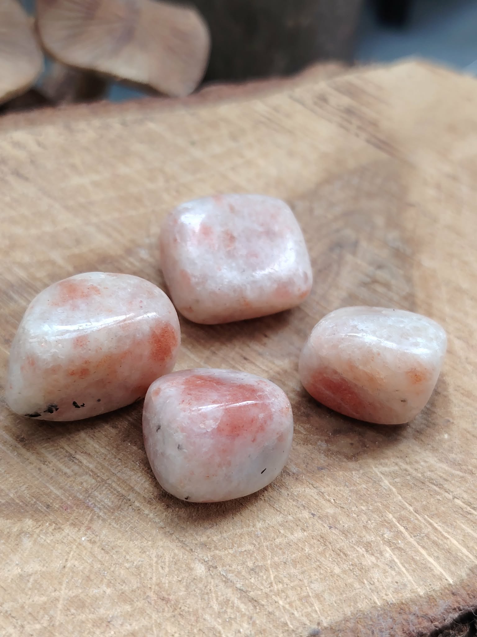 Quatre pierres roulées en pierre de soleil, posées sur une rondelle de bois, teintes crème et pêche, pour cultiver joie, confiance et vitalité.