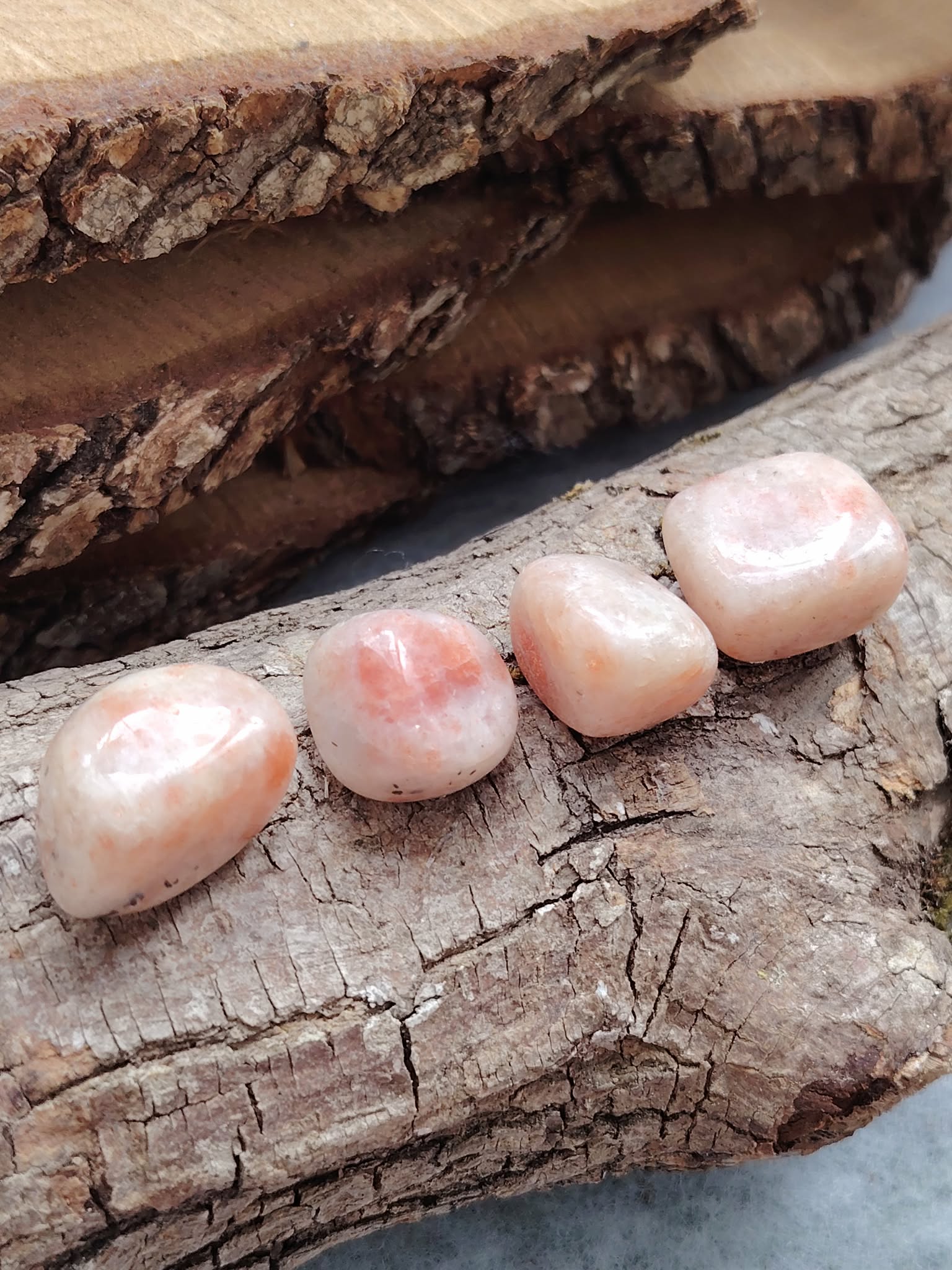 Quatre pierres roulées en pierre de soleil, posées sur une tranche de bois à l’écorce brute, lumière douce, pour la joie, la confiance et l’élan intérieur.