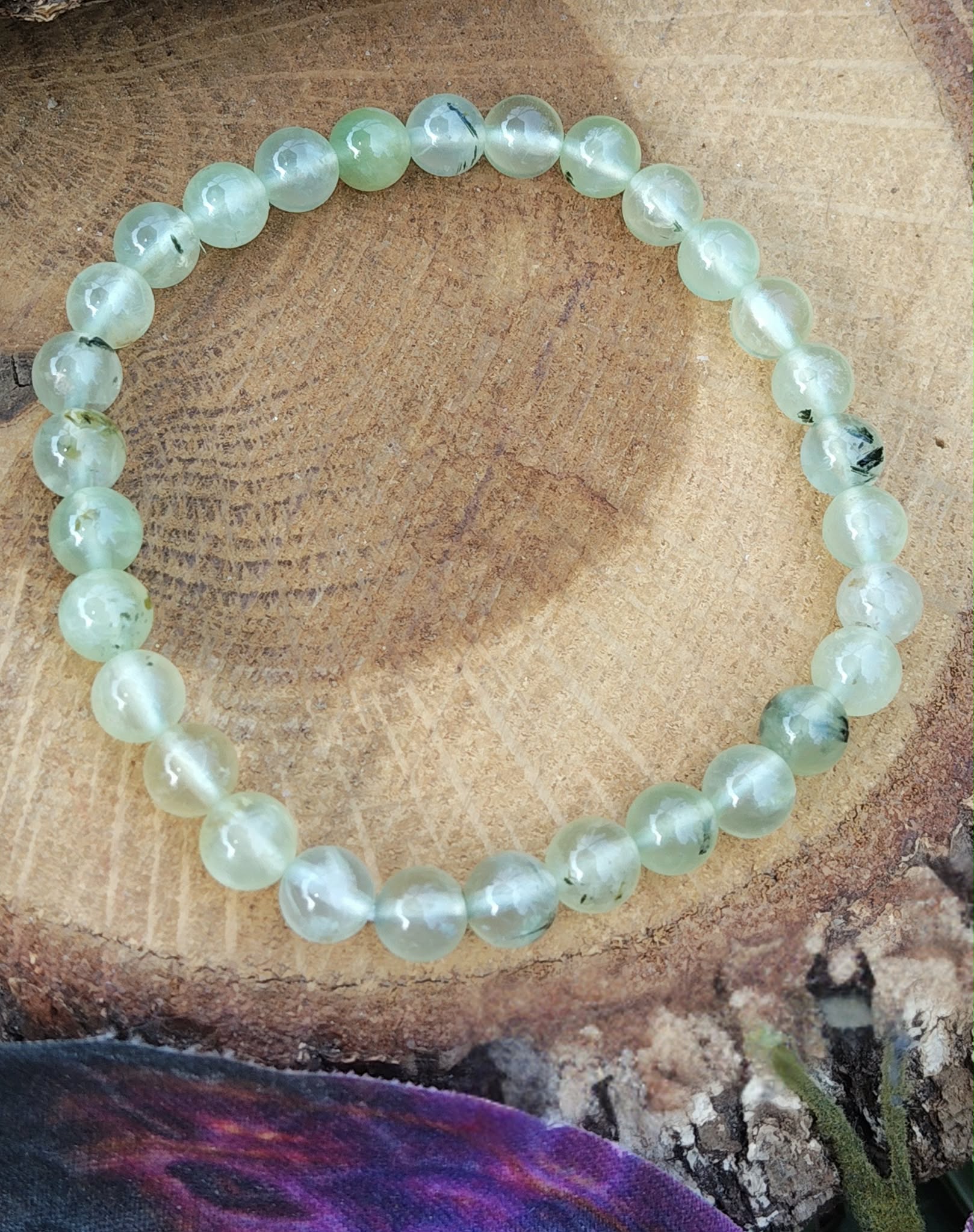 Bracelet préhnite 6 mm posé sur rondin de bois dans une ambiance douce, clarté mentale, équilibre émotionnel et respiration plus paisible