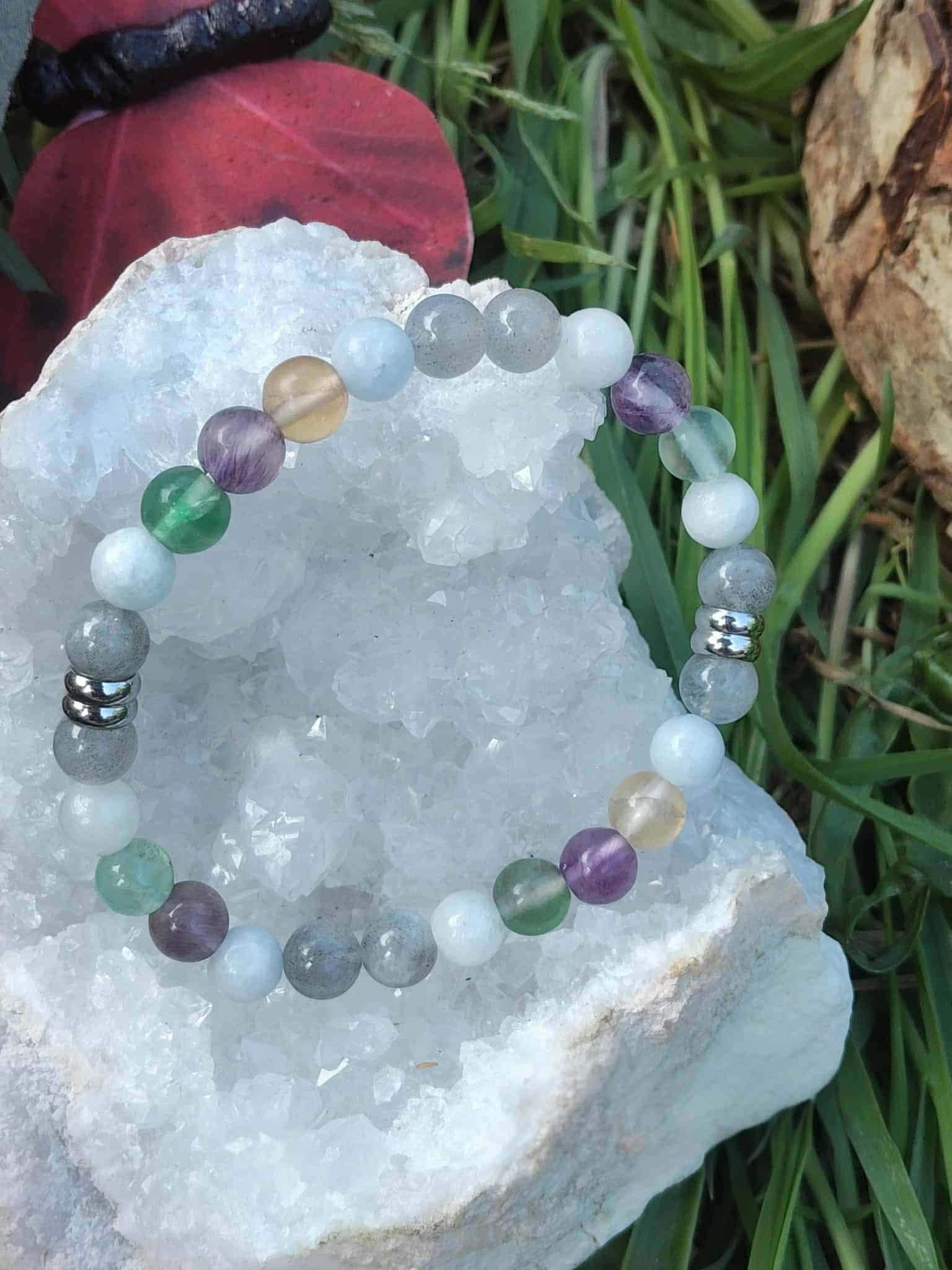 Bracelet pierres naturelles Énergie lunaire posé sur rondin de bois et feuillage vert, bijou ésotérique pour recentrage émotionnel