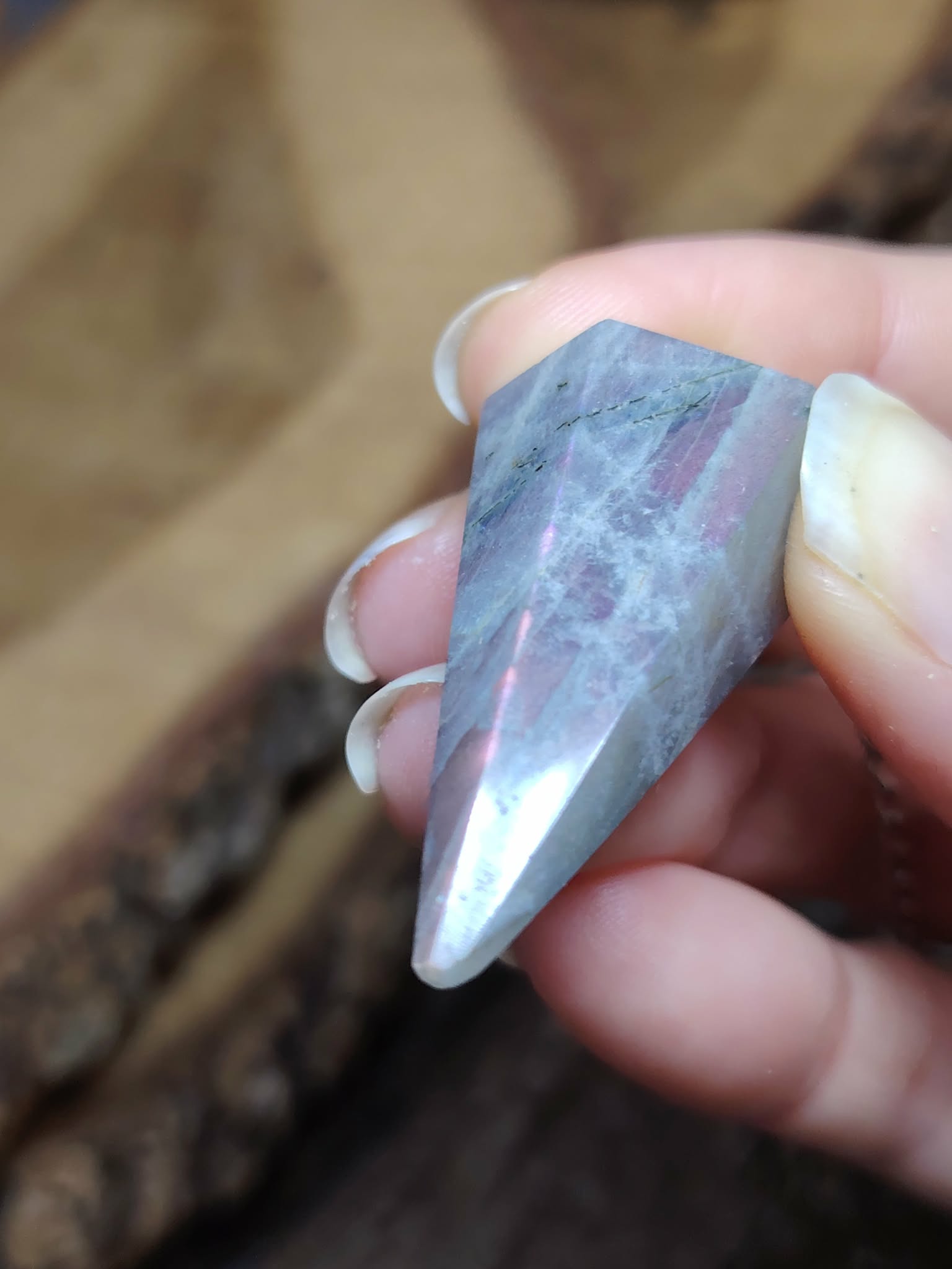 Pendule en labradorite arc-en-ciel tenu entre les doigts, sur fond de bois, reflets bleus et violets, pour protection douce et intuition.