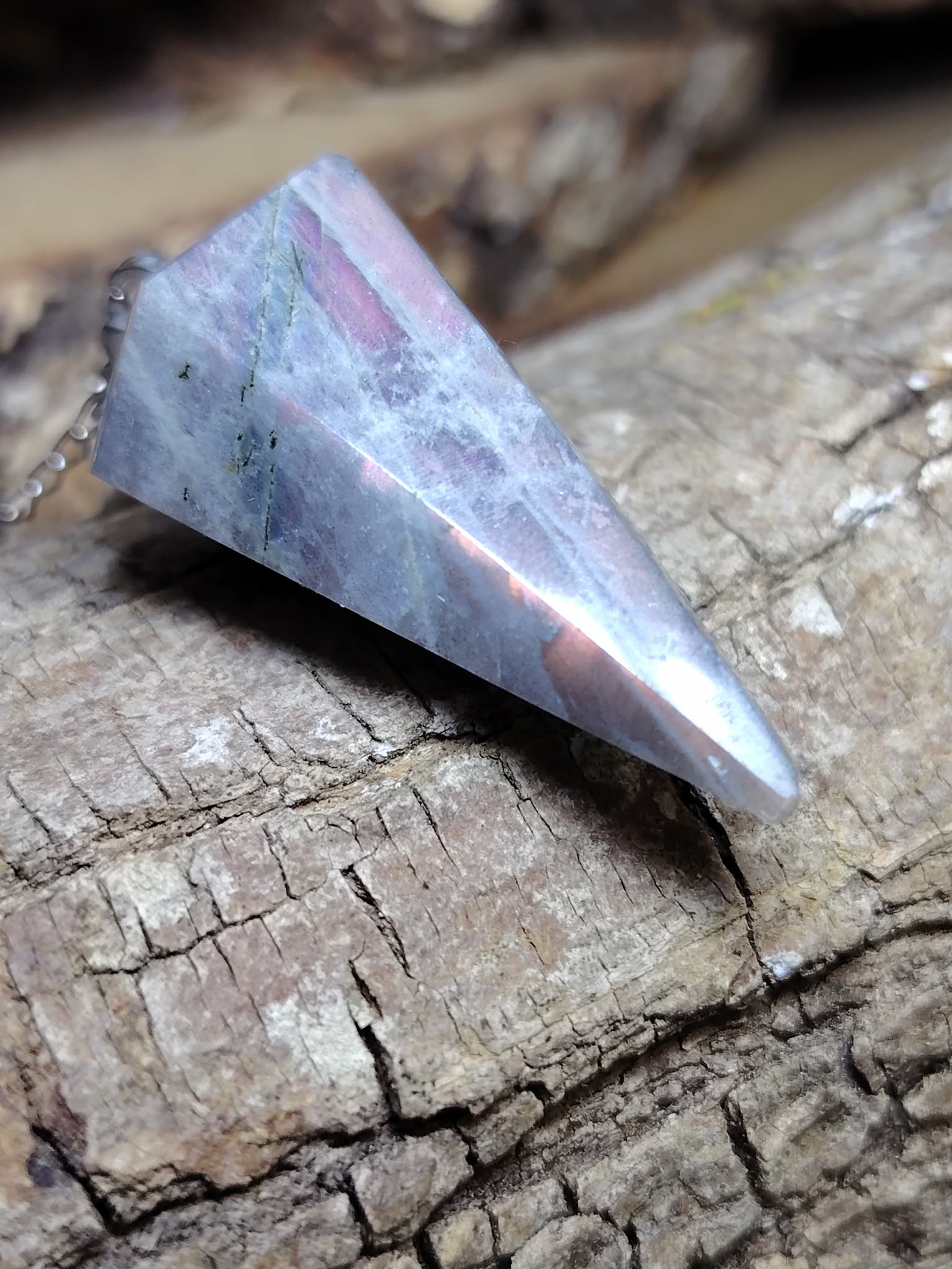 Pendule en labradorite arc-en-ciel posé sur écorce de bois, reflets bleus et violets, idéal pour la protection, l’ancrage et l’intuition.