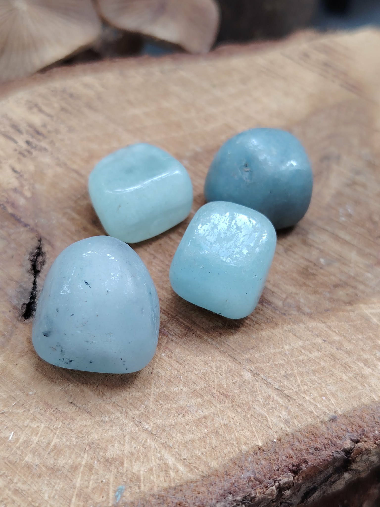 Quatre pierres roulées d’aigue-marine bleu pastel posées sur écorce et bois craquelé, ambiance nature, pour apaiser le mental et faciliter une communication douce. (