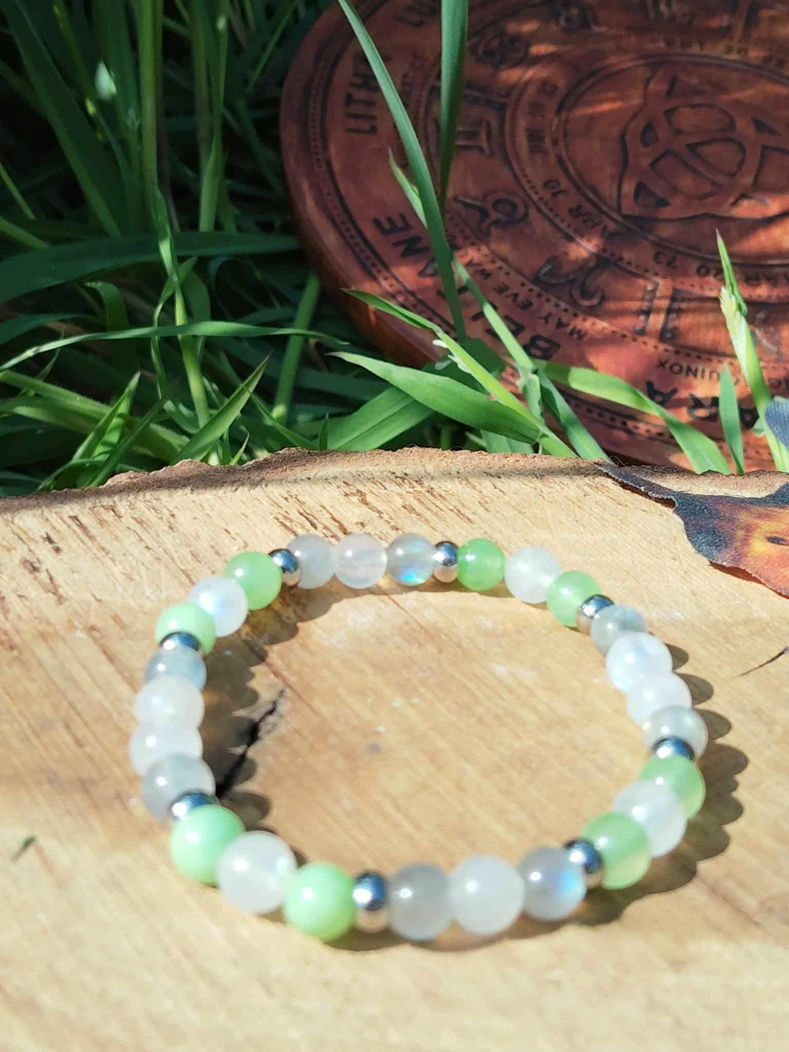 Bracelet endométriose sur rondin de bois avec herbes vertes en fond, jade vert, péristérite et labradorite pour soutien du féminin, sérénité et énergie plus douce