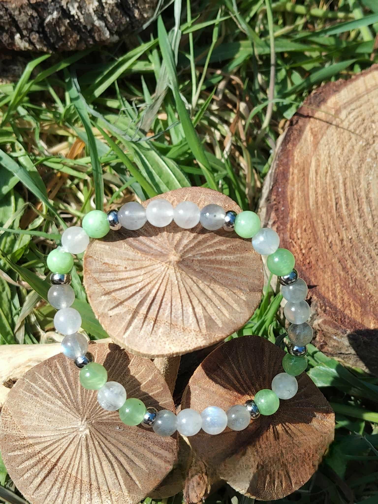 Bracelet endométriose posé sur deux champignons en bois devant feuillage vert, perles vert d’eau et bleutées pour calme intérieur, soutien émotionnel et recentrage