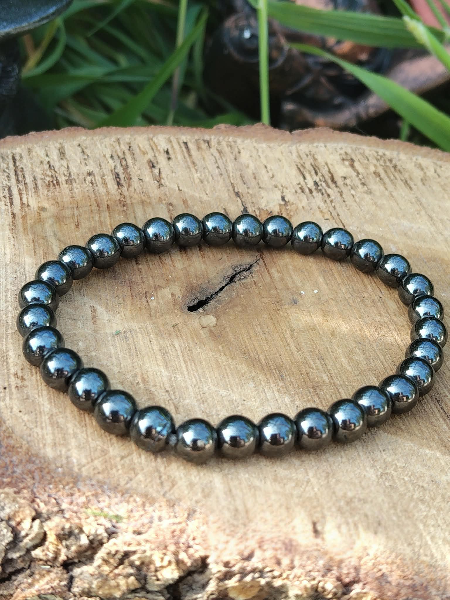 Bracelet hématite 6 mm en cercle sur tranche de bois avec herbes vertes, perles gris foncé métallisé pour volonté ferme, assurance et focus mental