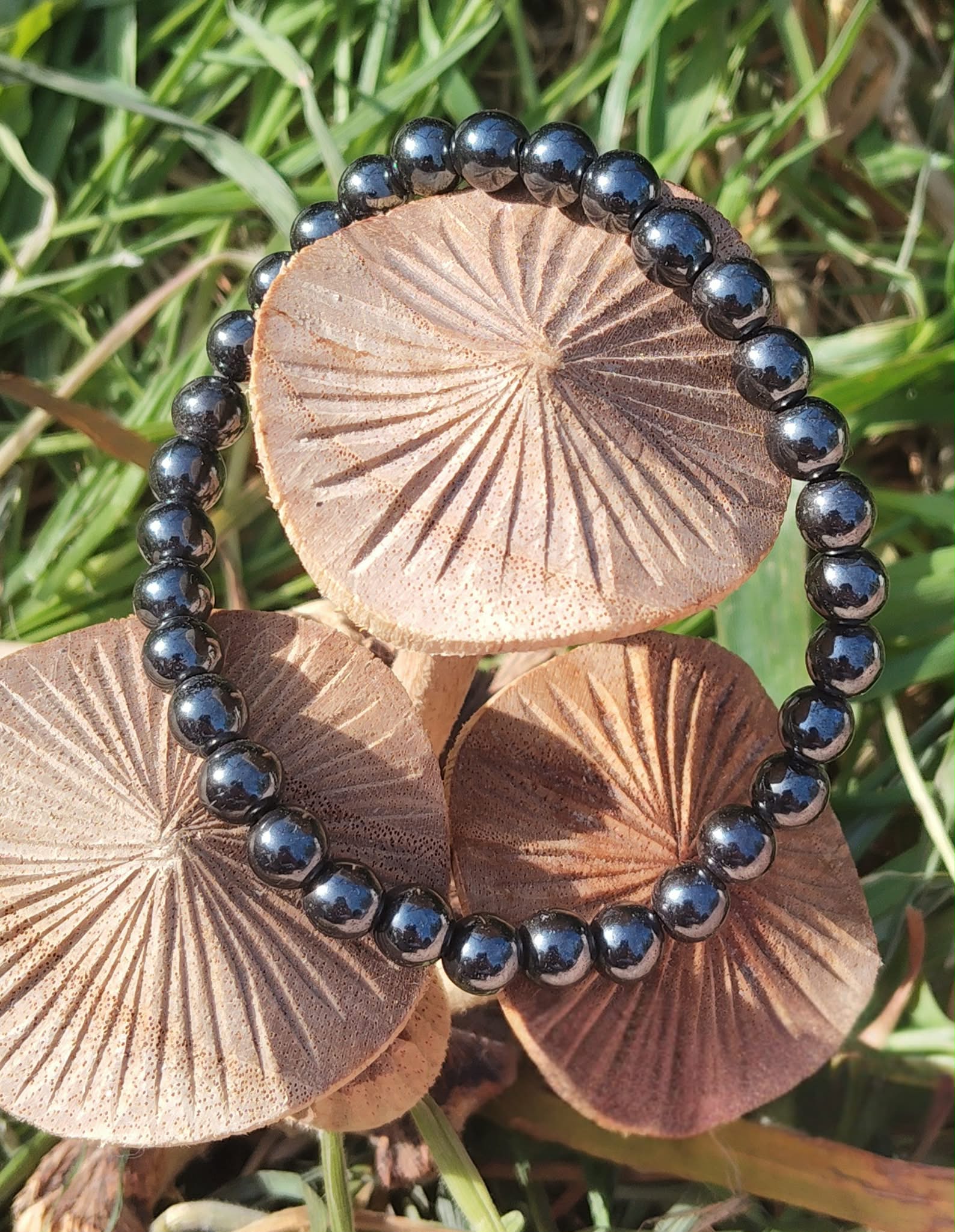 Bracelet hématite 6 mm autour de champignons sur herbe verte, perles anthracite brillantes pour aplomb, ancrage et énergie stable