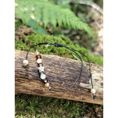 Bracelet cordon noir avec étoile dorée et perles facettées crème, ambrées et rosées, présenté à plat avec ses liens réglables.