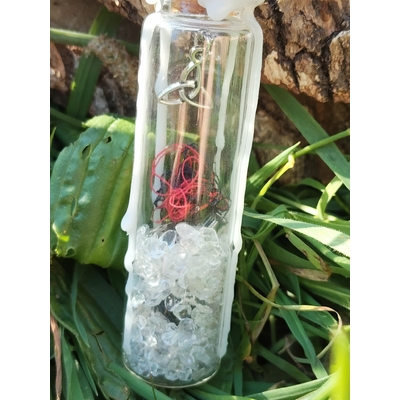 Spell jar en fiole de verre avec cristal de roche, fil rouge, cire blanche et breloque triquetra, photo en extérieur, énergie de protection et clarté.