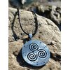 Pendentif Triskell sur cordon noir posé sur rochers en Bretagne, symbole celtique des cycles de vie et du mouvement continu