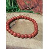 Bracelet jaspe rouge 6 mm sur tranche de bois avec herbes vertes et décor ésotérique, perles rouge brique pour courage posé, ancrage et présence solide