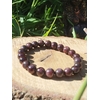 Bracelet grenat 8 mm en perles rondes bordeaux posé sur rondin de bois en extérieur, bijou en pierre naturelle pour ancrage et vitalité.