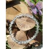 Bracelet cristal de roche 6 mm en gros plan sur fond champignons en bois, perles translucides polies pour amplification des intentions et lucidité