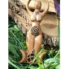 Statuette Gaïa déesse en bois avec spirale, posée dans un décor végétal (mousse/plantes) contre une écorce, ambiance nature; inspire ancrage, apaisement, protection douce, intuition et harmonie.