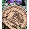 Dessous de plat rond en liège, loup gravé, bordure celtique; photo dans l’herbe, ombres de feuilles. Symbolique: instinct, protection, loyauté