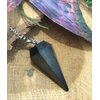 Pendule en shungite noire sur rondin de bois, décor naturel witchy, chaîne argentée, radiesthésie/divination, ancrage, protection, purification, clarté mentale, apaisement • Magic Gaïa