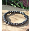 Bracelet Pierre de Lave 6 mm sur élastique, perles noires poreuses sur tranche de bois avec herbes, ancrage et force intérieure.