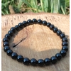 Bracelet Onyx noir en perles rondes sur élastique, posé sur tranche de bois avec herbes vertes, aplomb, constance et sang-froid.