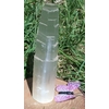 Tour en sélénite translucide photographiée en extérieur sur fond d’herbe, avec un papillon violet au bas de l’image, ambiance douce et apaisante.