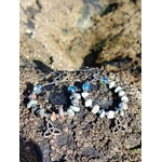 Boucles d’oreilles Magic Gaïa en larimar et aqua aura posées sur rocher granitique en Bretagne, perles bleu ciel et blanches en cercle avec triquetra, ambiance minérale naturelle évoquant douceur, intuition et apaisement