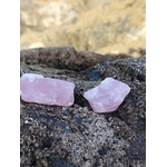 Deux quartz rose bruts posés sur rocher sombre en Bretagne avec falaises beiges floues en arrière-plan, pierres naturelles reliées à la tendresse, au calme du cœur et à l’apaisement intérieur.