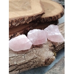 Trois quartz rose bruts posés sur tranche de bois et rocher, lumière douce naturelle et décor bohème, pierres naturelles liées à la bienveillance, à la douceur affective et à l’équilibre intérieur.